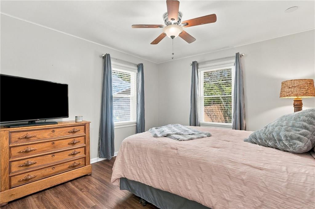 Bedroom with a pink bedspread, two curtained windows, and a wooden dresser with a television.