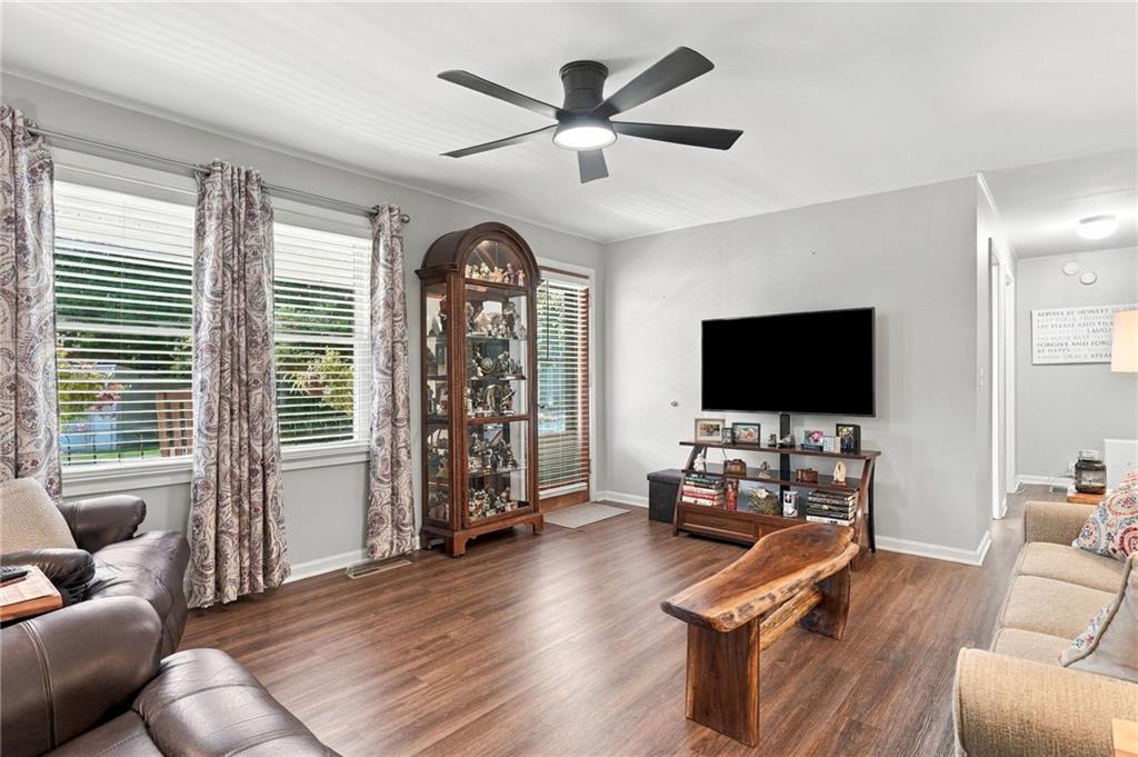 Living room with wood flooring, patterned curtains, a display cabinet, and ceiling fan.