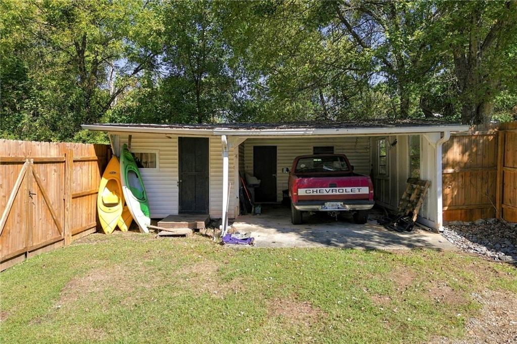 Covered carport beside a single-story home, with a pickup truck and kayaks.