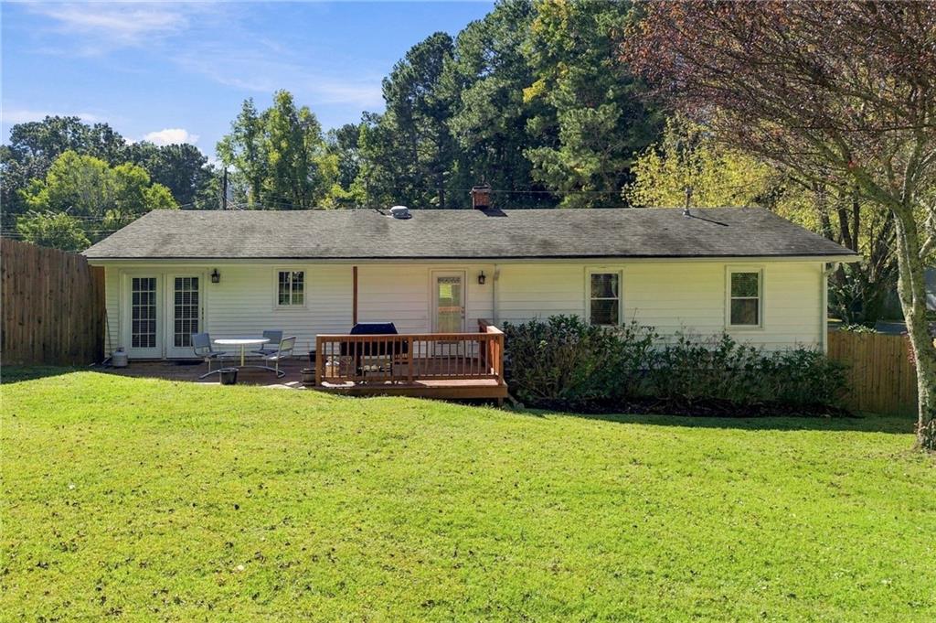 Rear exterior of a single-story white home with a small wooden deck and broad lawn.
