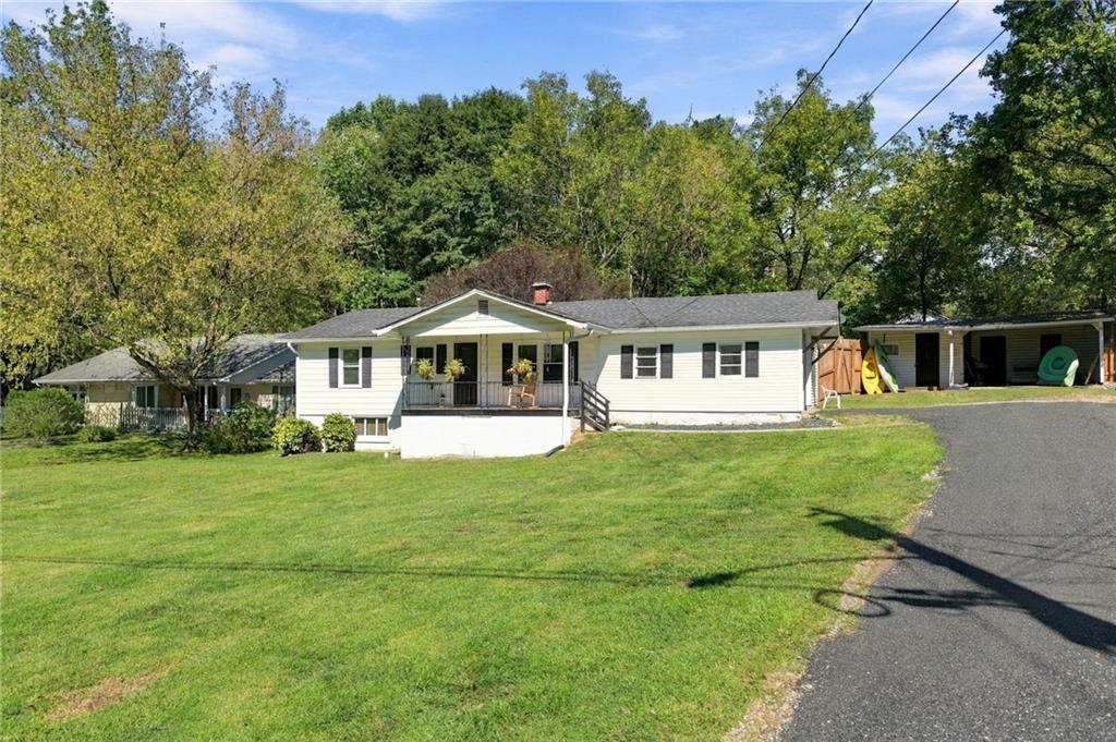 Single-story white home with a covered porch, broad lawn, and wooded backdrop.