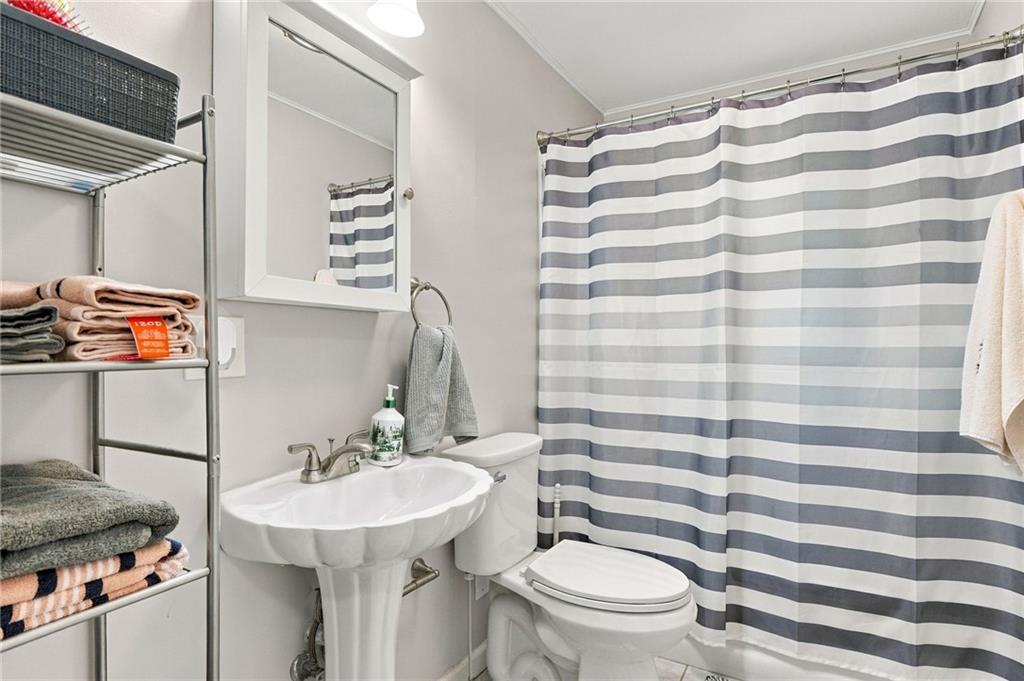 Bathroom with a pedestal sink, toilet, and gray-and-white striped shower curtain.