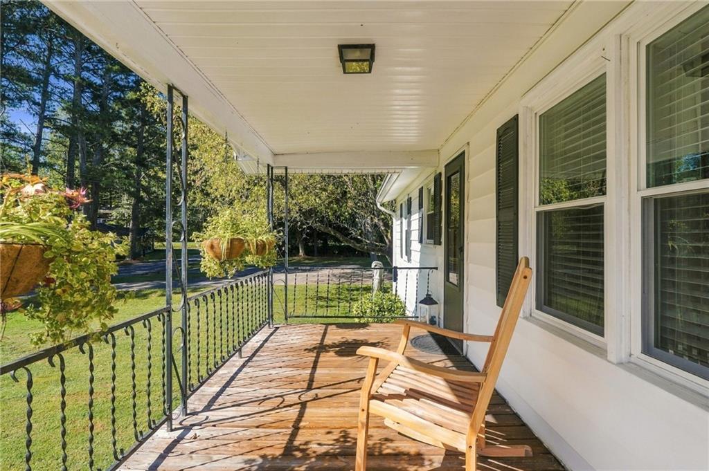 Covered front porch with a wooden rocking chair, decorative iron railing, and wooded yard beyond.