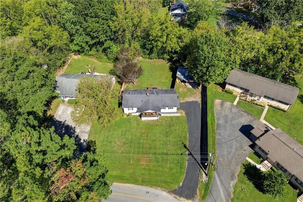 Aerial view of a single-story home with a broad lawn, driveway, and surrounding trees.