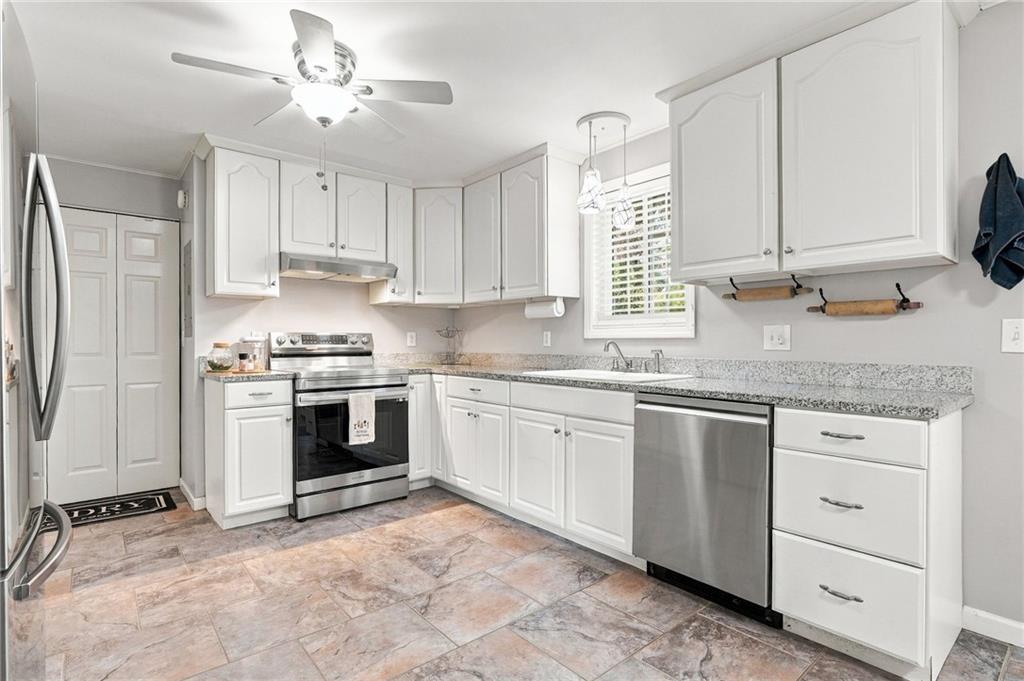 Bright kitchen with white cabinets, granite counters, stainless steel appliances, and a ceiling fan.