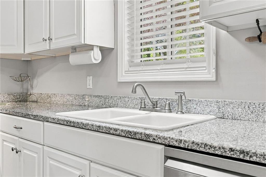 Kitchen sink with granite counters, white cabinets, and a window with blinds.