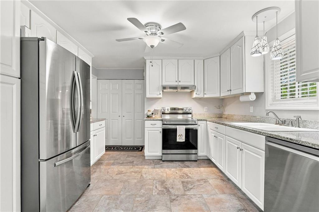 Bright kitchen with white cabinets, stainless steel appliances, granite counters, and a window with blinds.