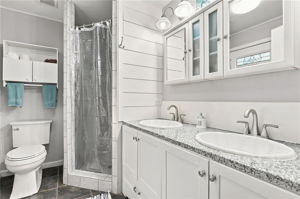 Bathroom with a double-sink vanity, granite countertop, and glass-enclosed shower.