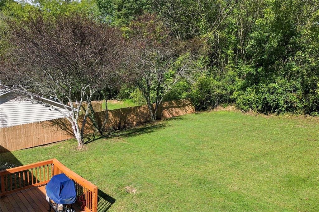 Backyard lawn bordered by a wooden fence and trees, with a raised deck and covered grill.