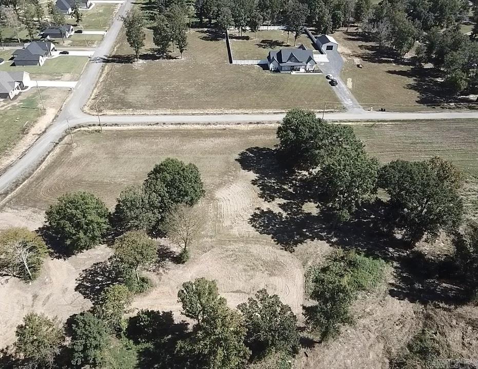 Aerial view of a cleared lot with scattered trees, neighboring homes, and roads.