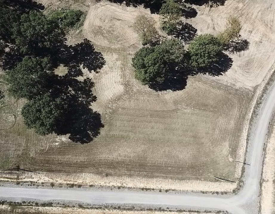 Aerial view of a cleared vacant lot with mature trees beside a curving road.