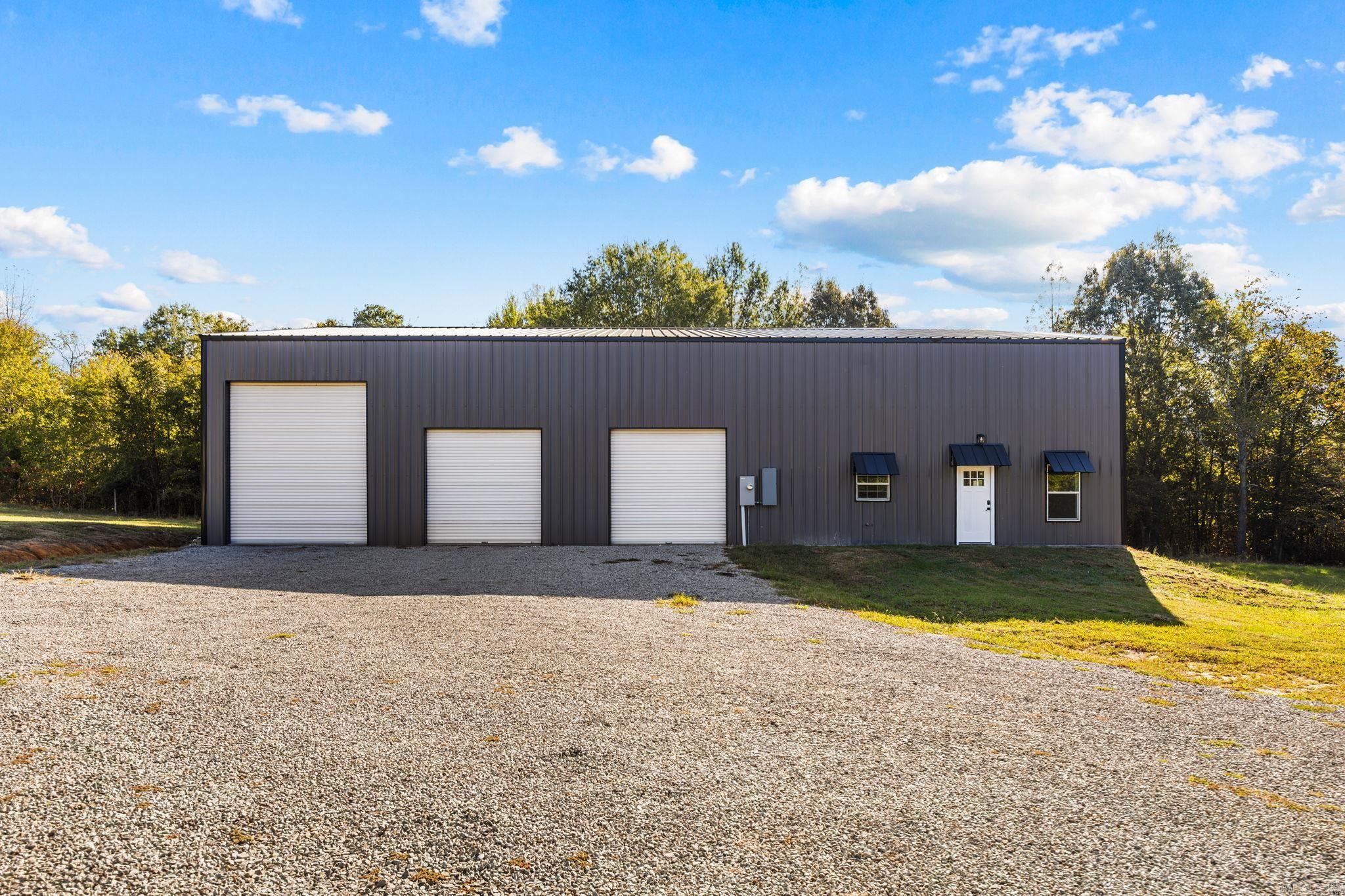 Dark metal workshop with three roll-up doors and a gravel driveway.