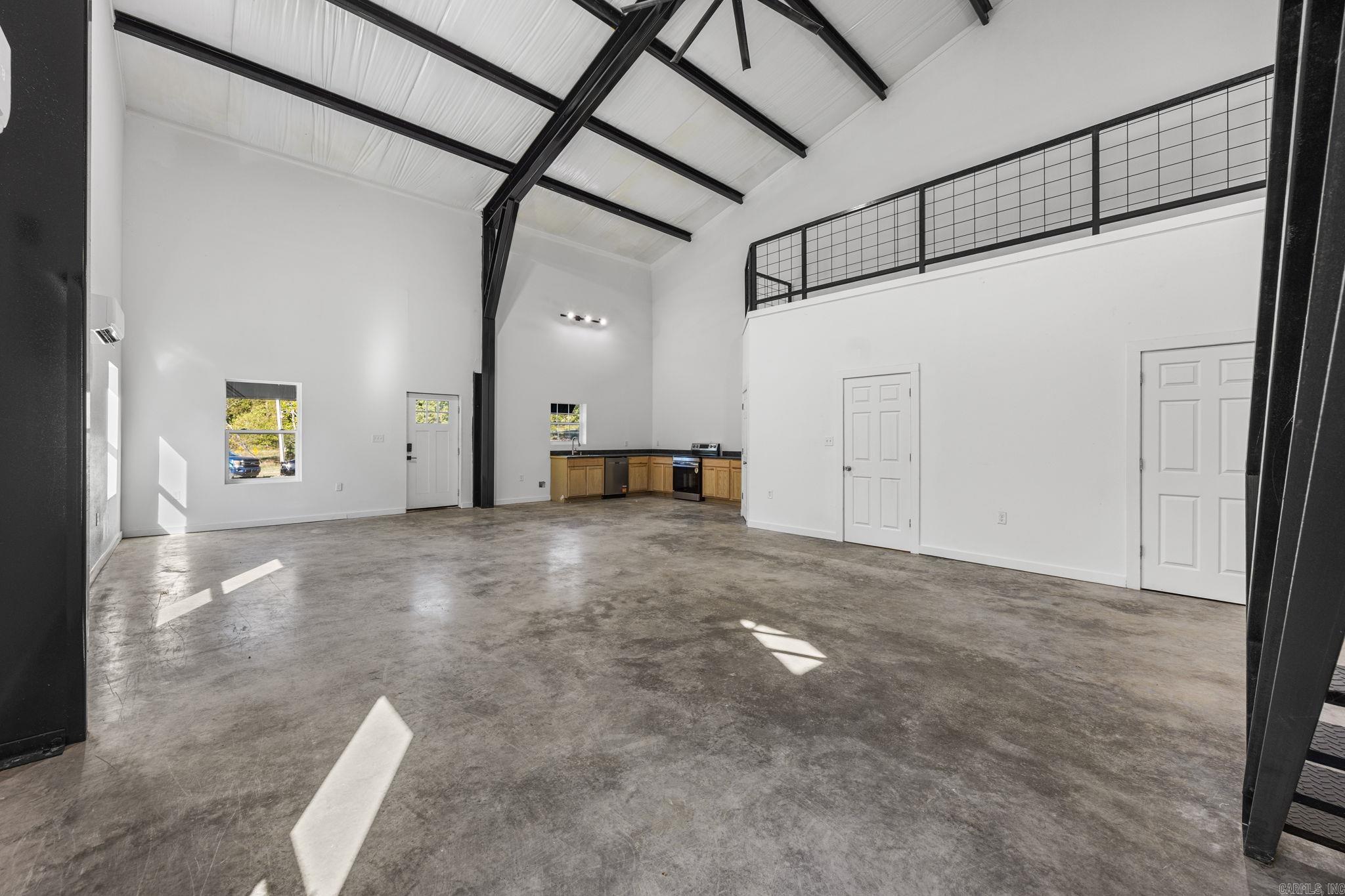 Open-plan living space with a compact kitchen, polished concrete floor, and vaulted ceiling with exposed beams.