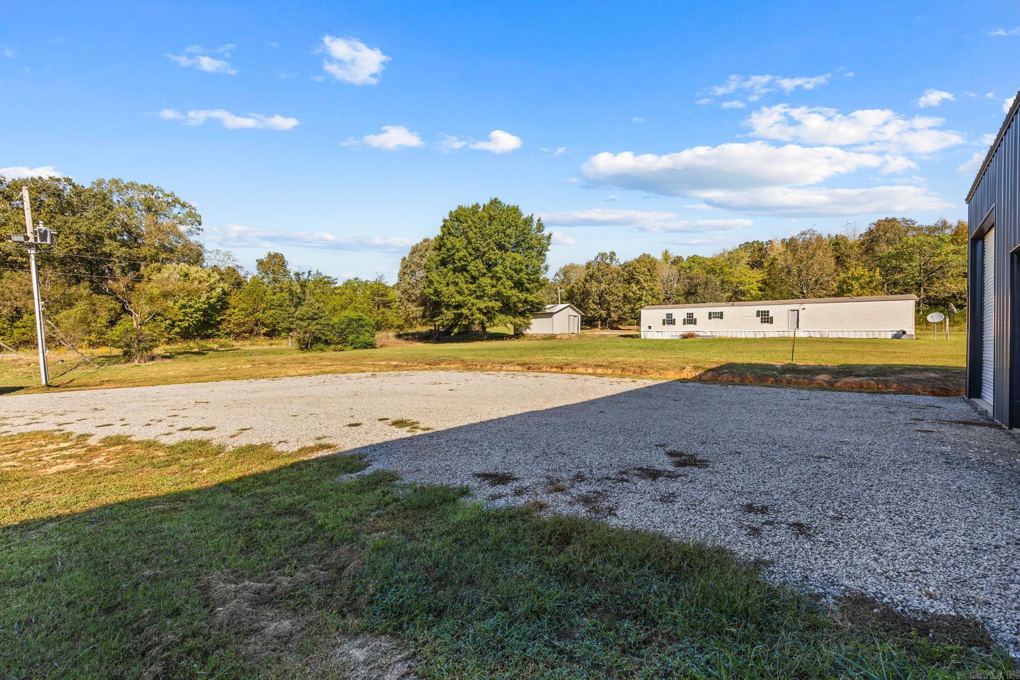 Gravel driveway and grassy yard with a manufactured home, shed, and metal building.