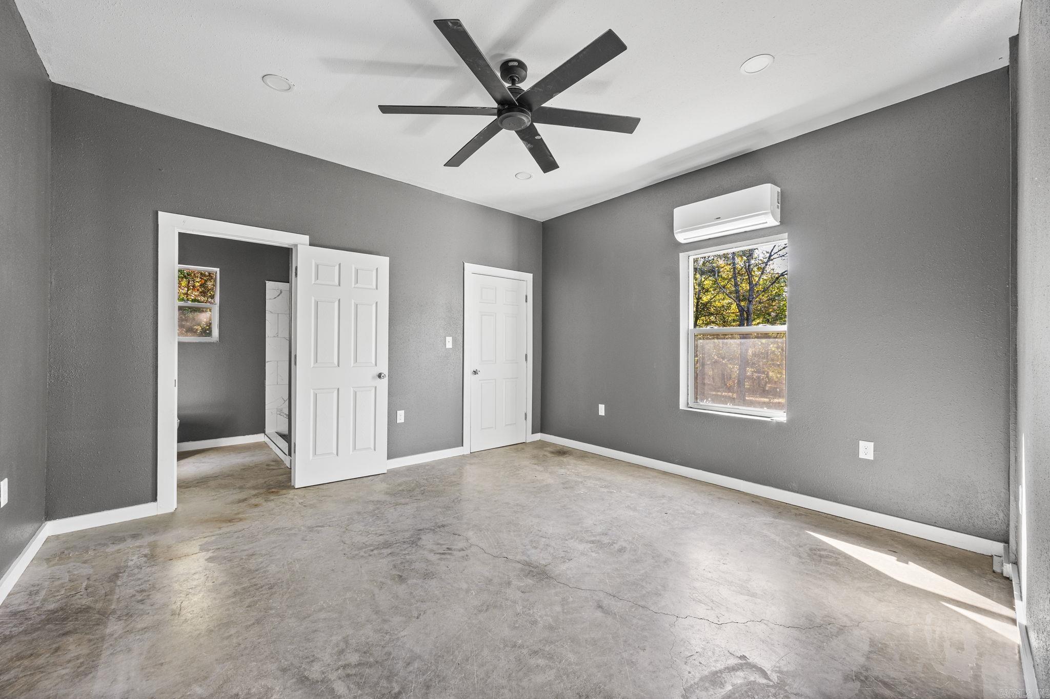 Empty bedroom with gray walls, a concrete floor, ceiling fan, and wall-mounted air conditioner.
