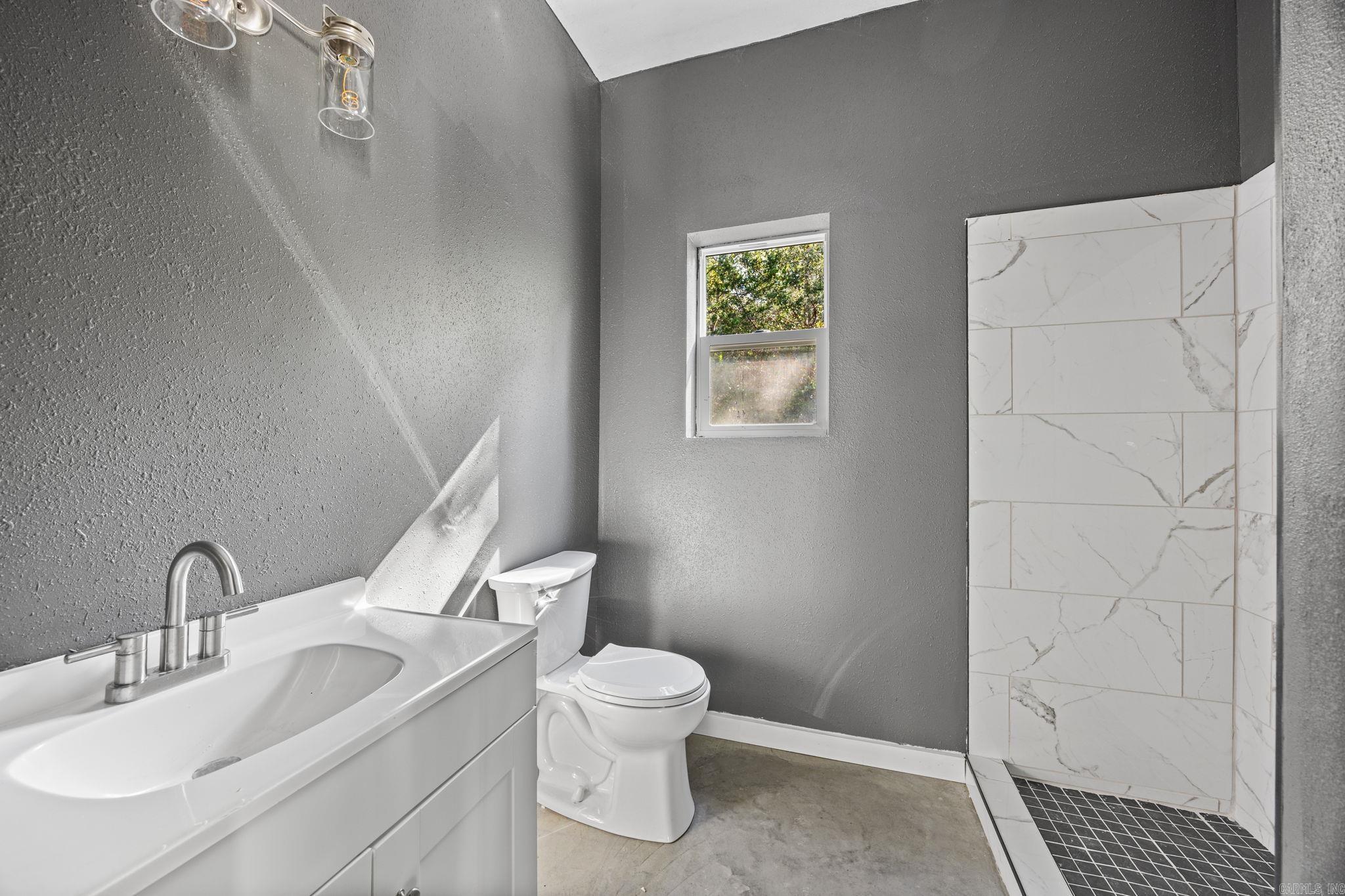 Bathroom with a white vanity, toilet, and marble-look tiled walk-in shower.