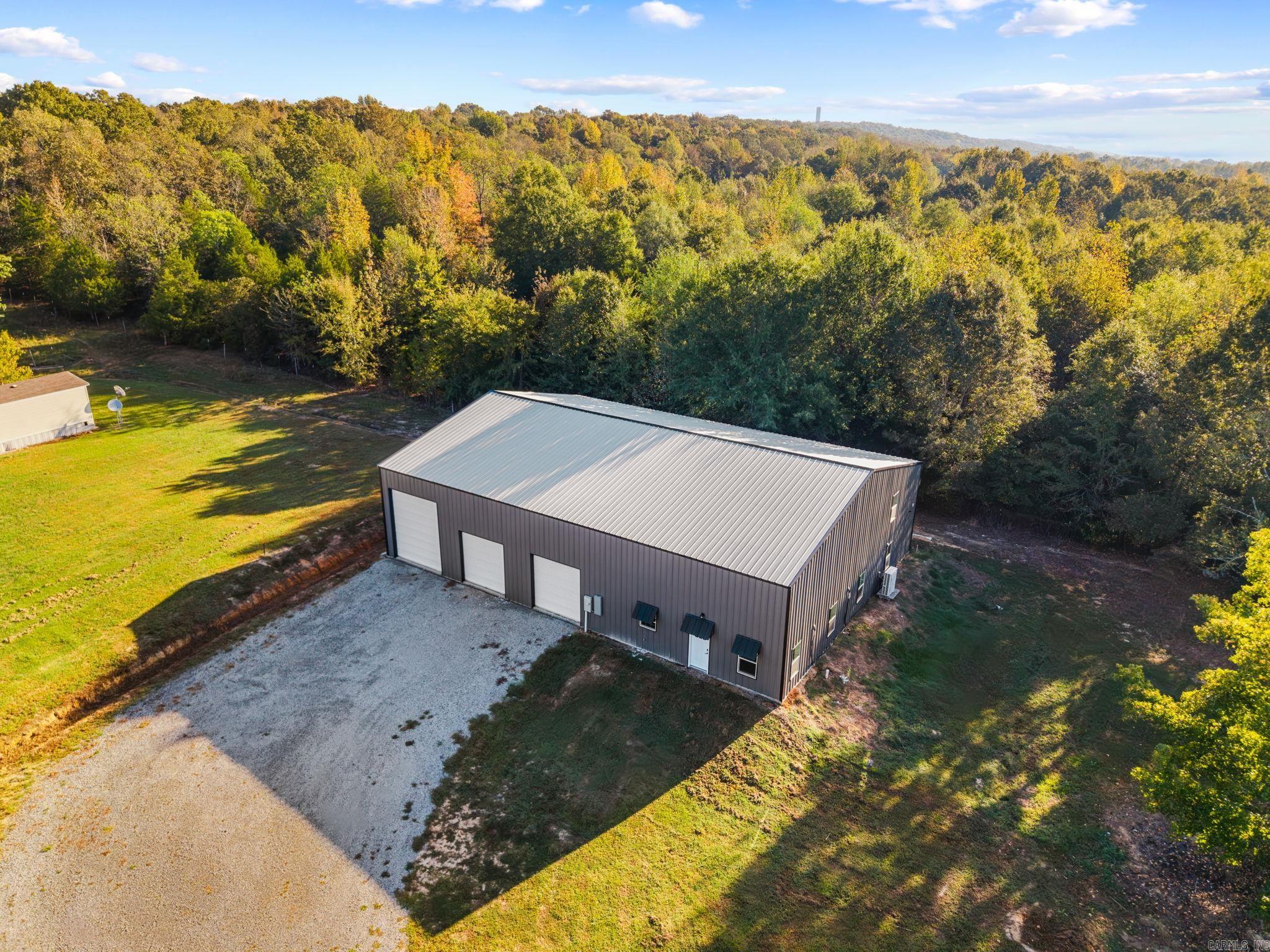 Aerial view of a metal-sided building with gravel parking and wooded surroundings.