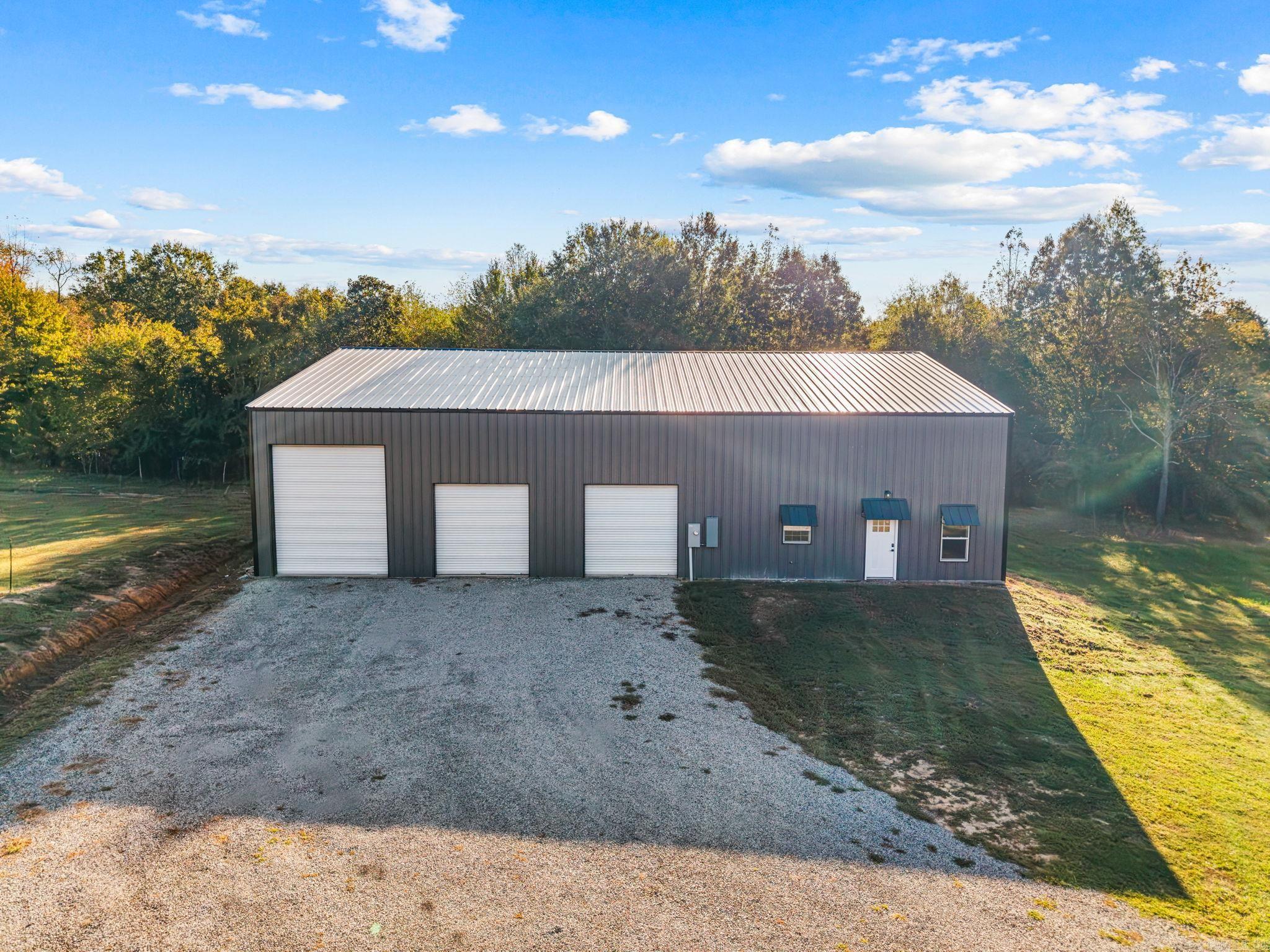 Gray metal workshop with three roll-up doors beside a broad gravel driveway.