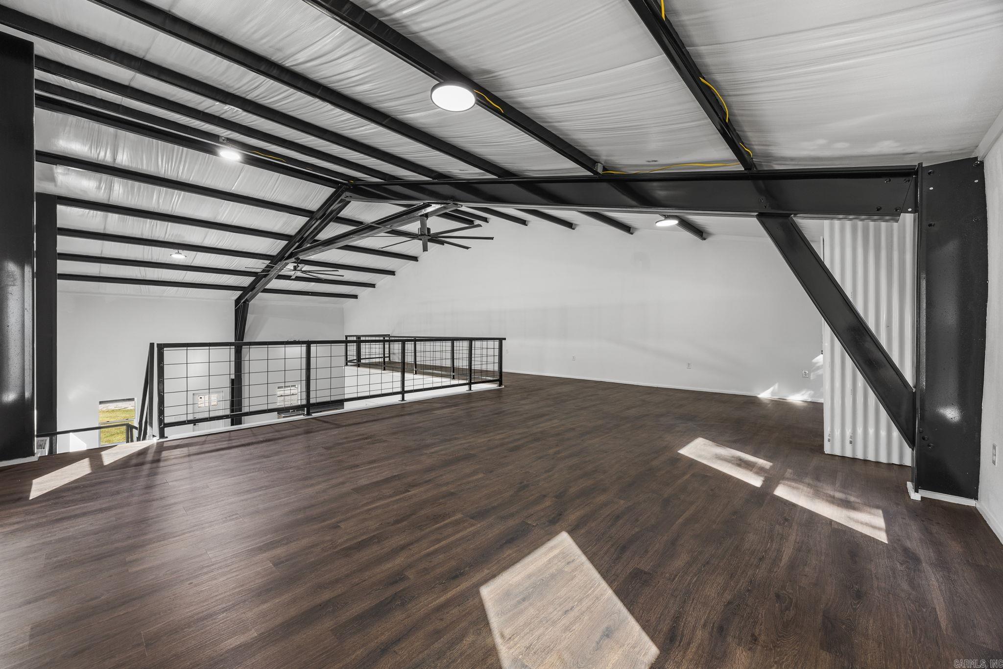 Open loft with dark wood flooring, black steel beams, and a metal railing.