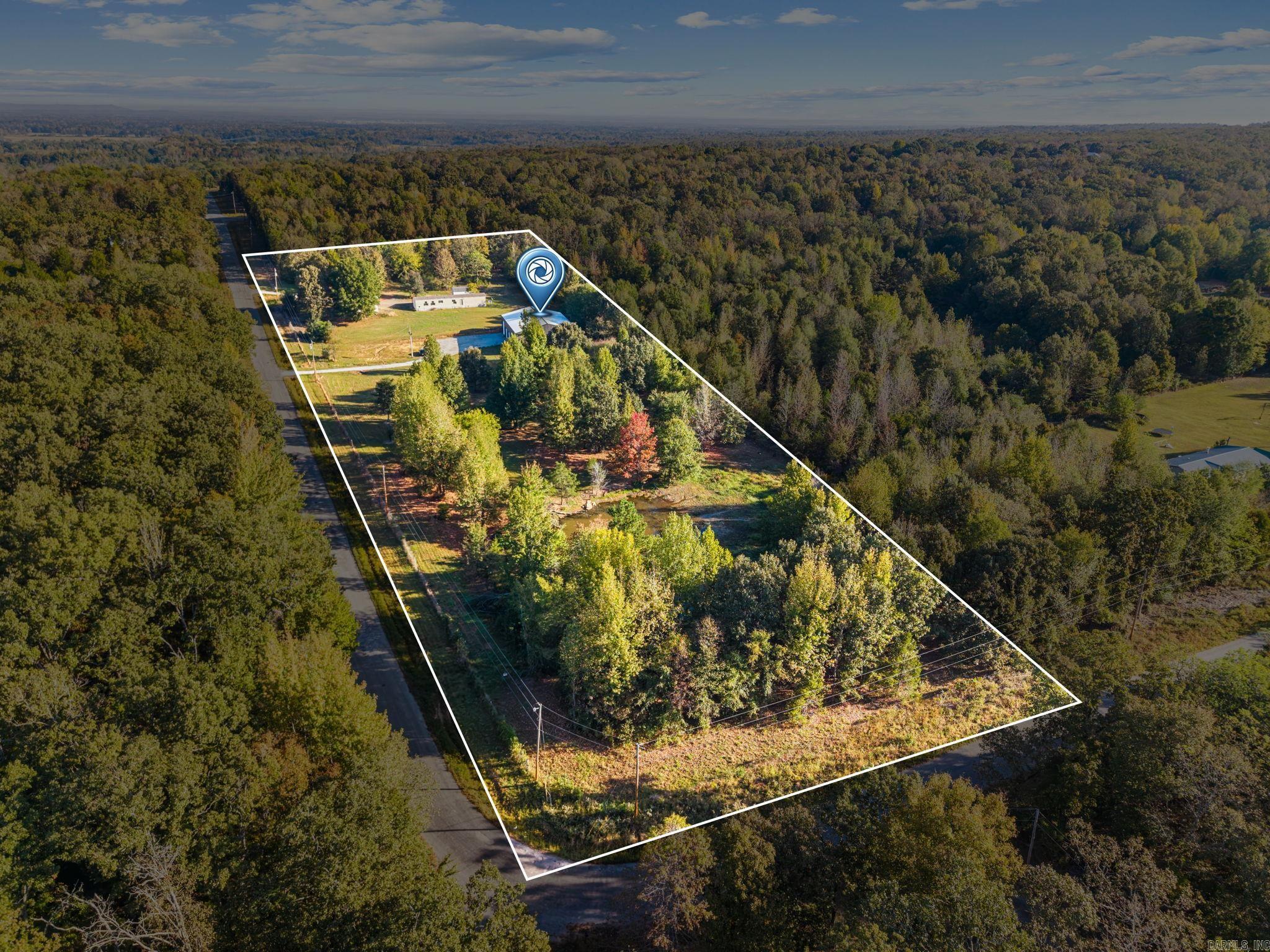 Aerial view of a wooded property outlined by boundary lines, with a road and buildings.