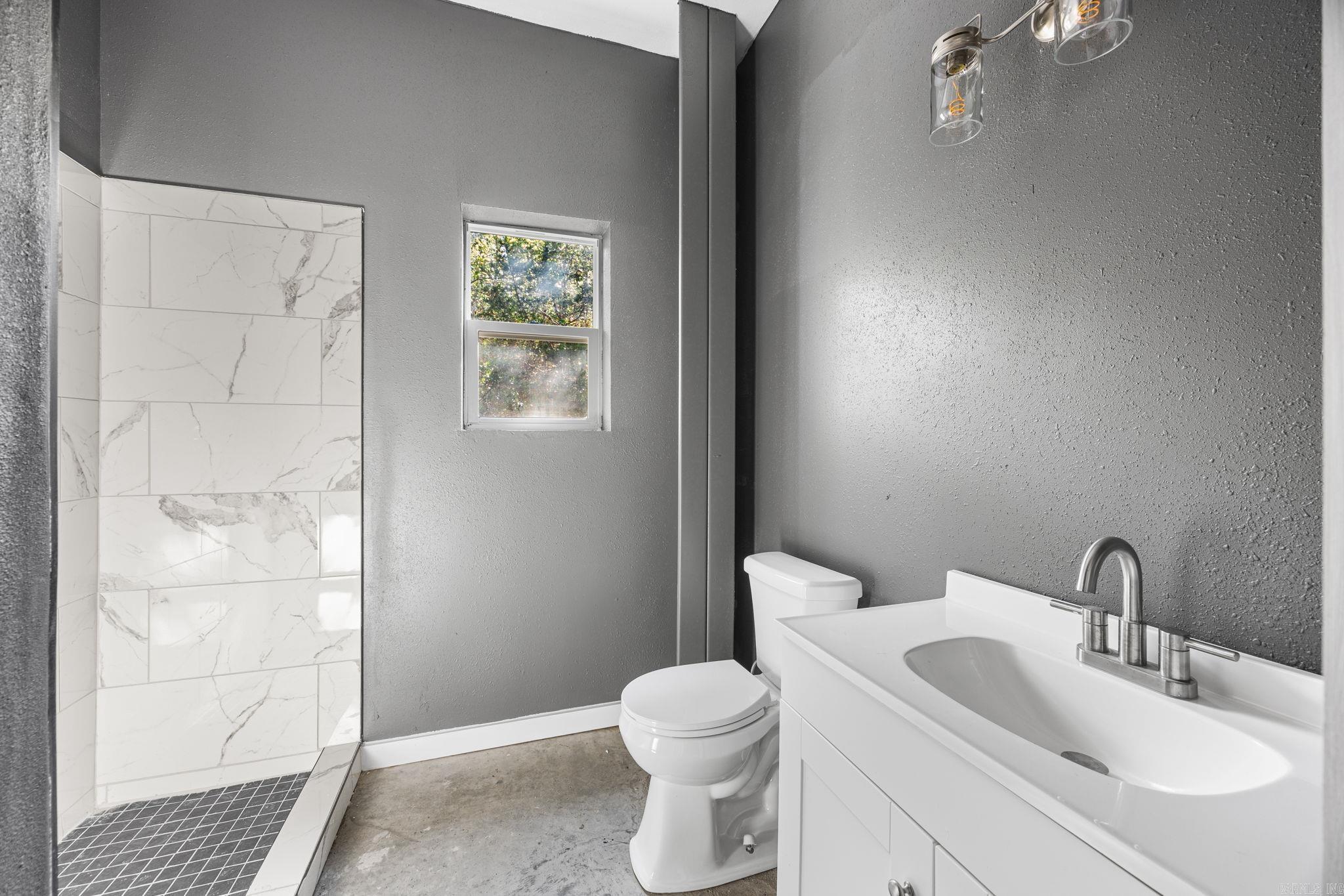 Bathroom with a tiled walk-in shower, white vanity, toilet, and small window.