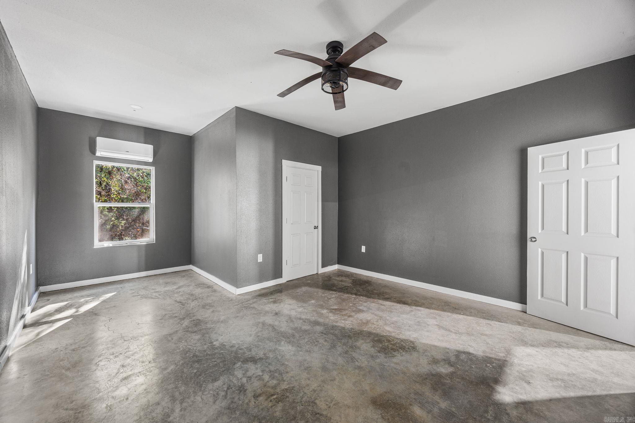 Vacant bedroom with gray walls, a concrete floor, ceiling fan, and window-mounted air conditioner.