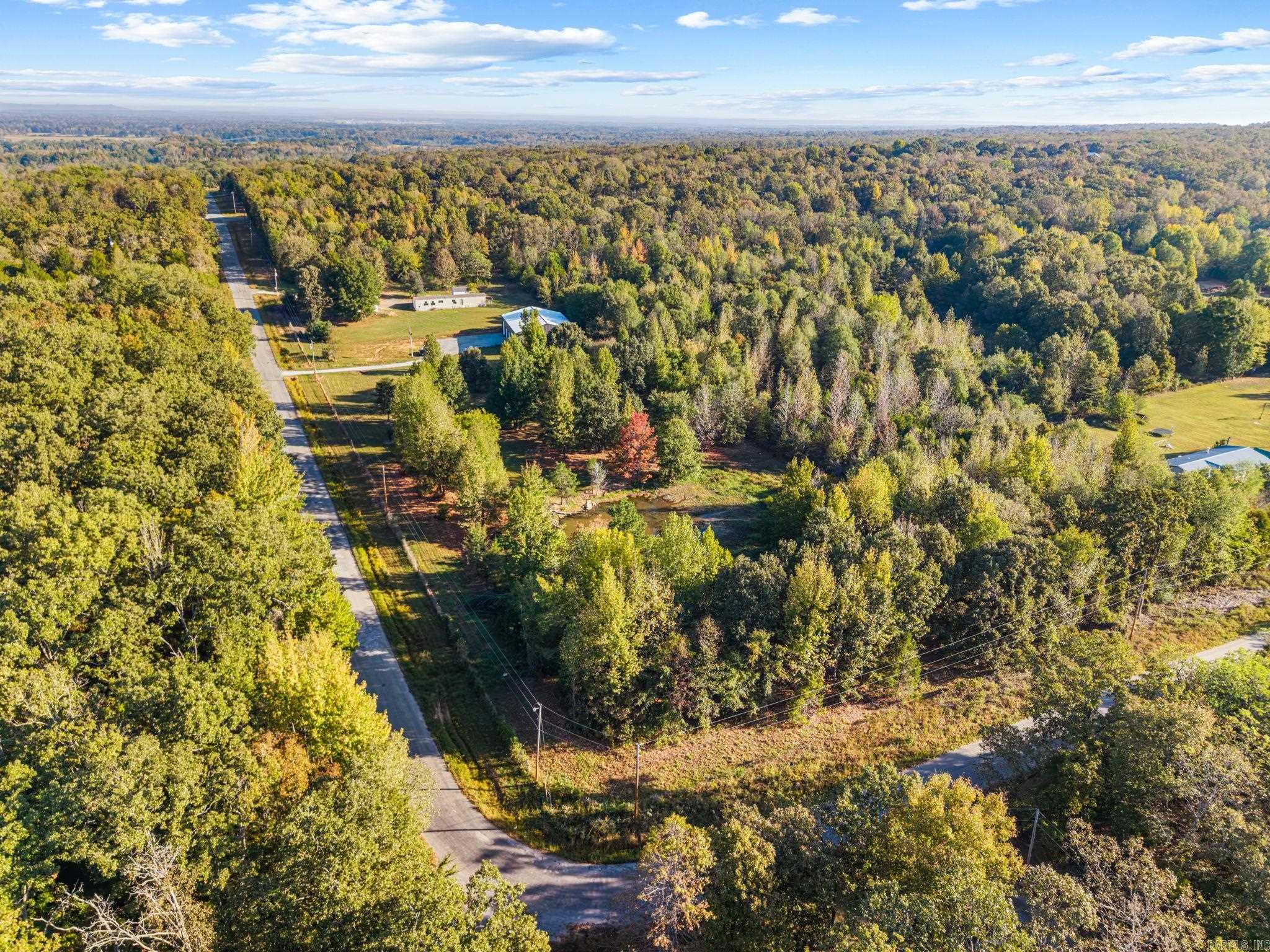Aerial view of a wooded property with a road, open clearing, and scattered buildings.