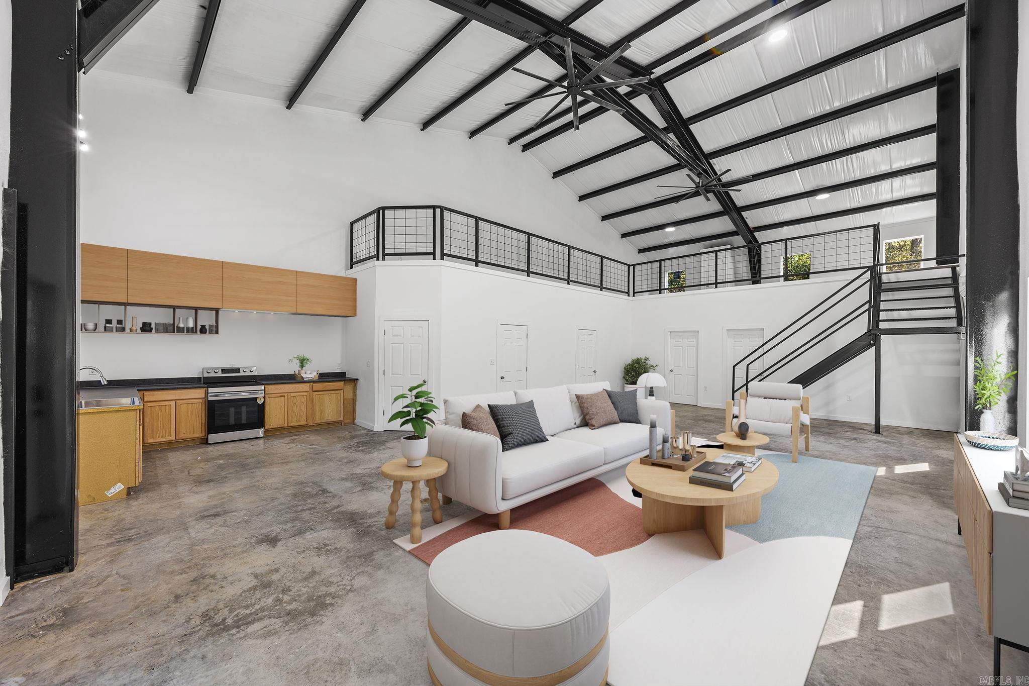 Open-concept living room and kitchen with a high vaulted ceiling, exposed beams, and a mezzanine.