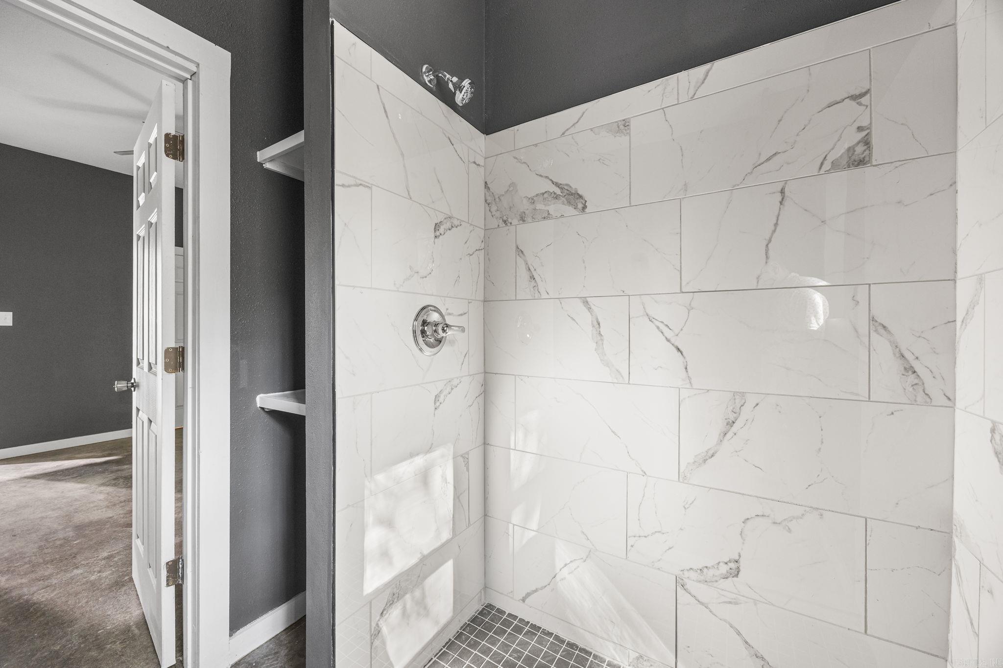 Walk-in shower with large veined marble-look tiles, dark walls, and a small mosaic floor.