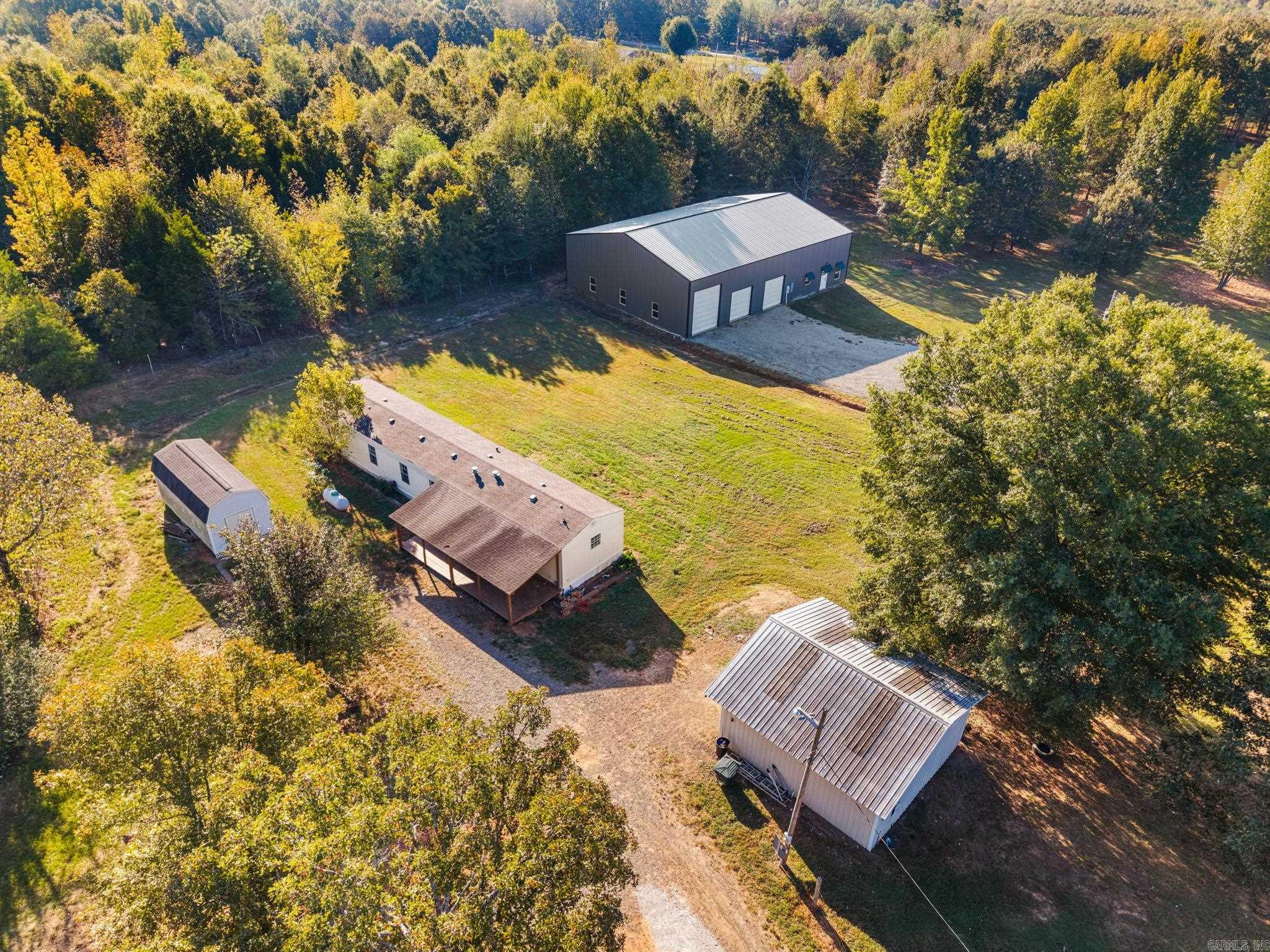 Aerial view of a wooded property with a home, detached sheds, and a large metal workshop.