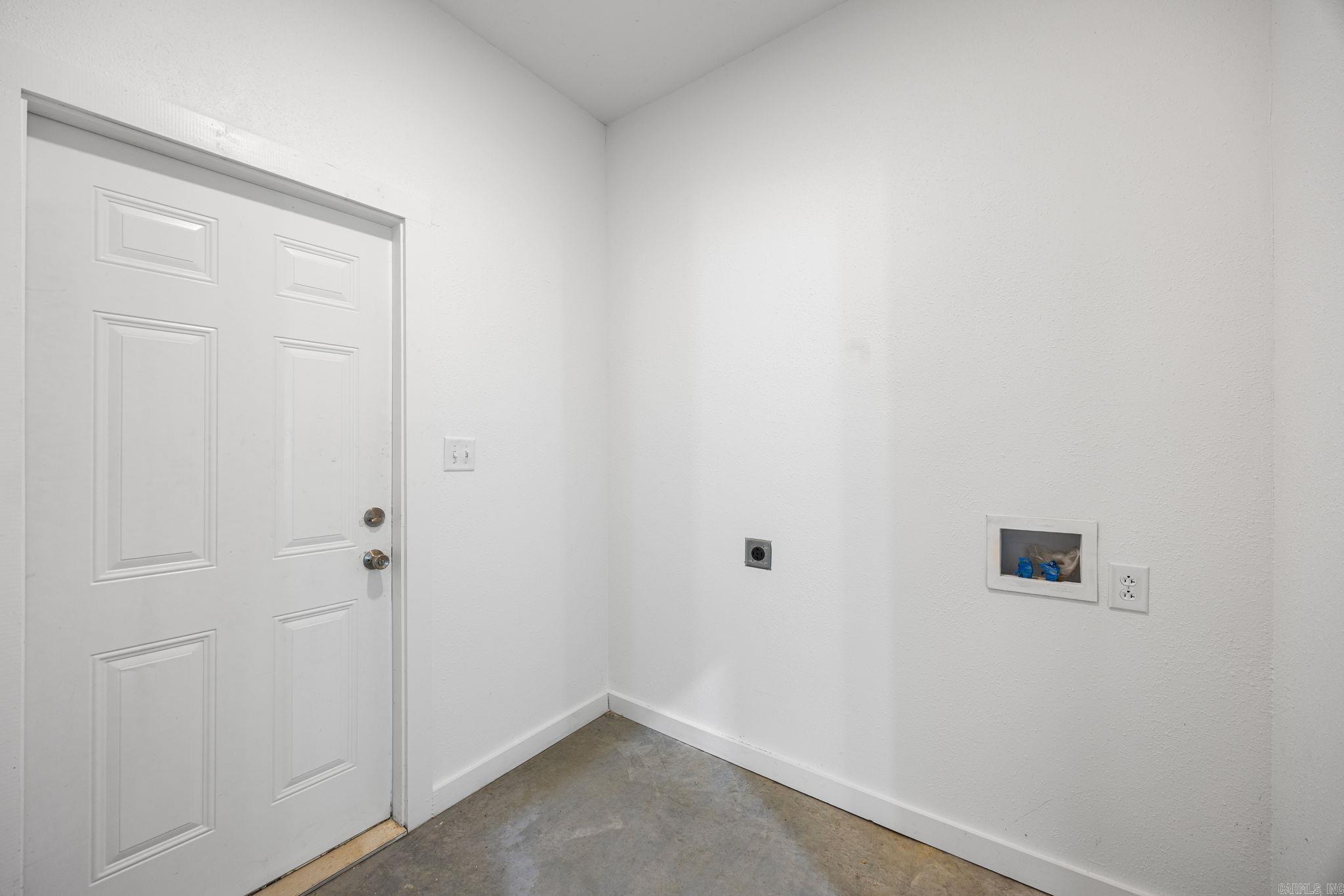 Bare laundry area with washer hookups, a white door, and concrete flooring.