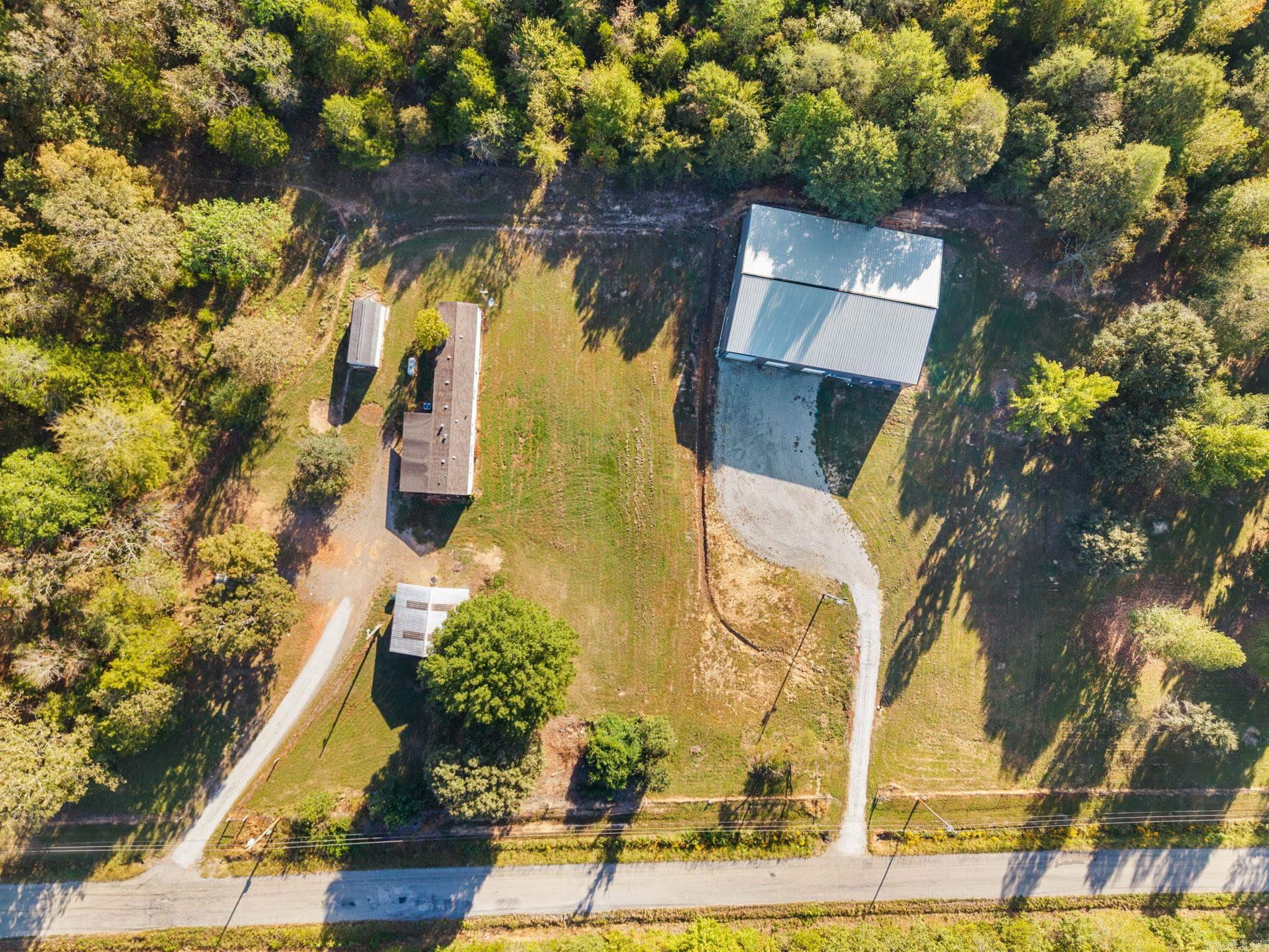 Aerial view of a wooded property with a home, large metal outbuilding, and gravel driveways.