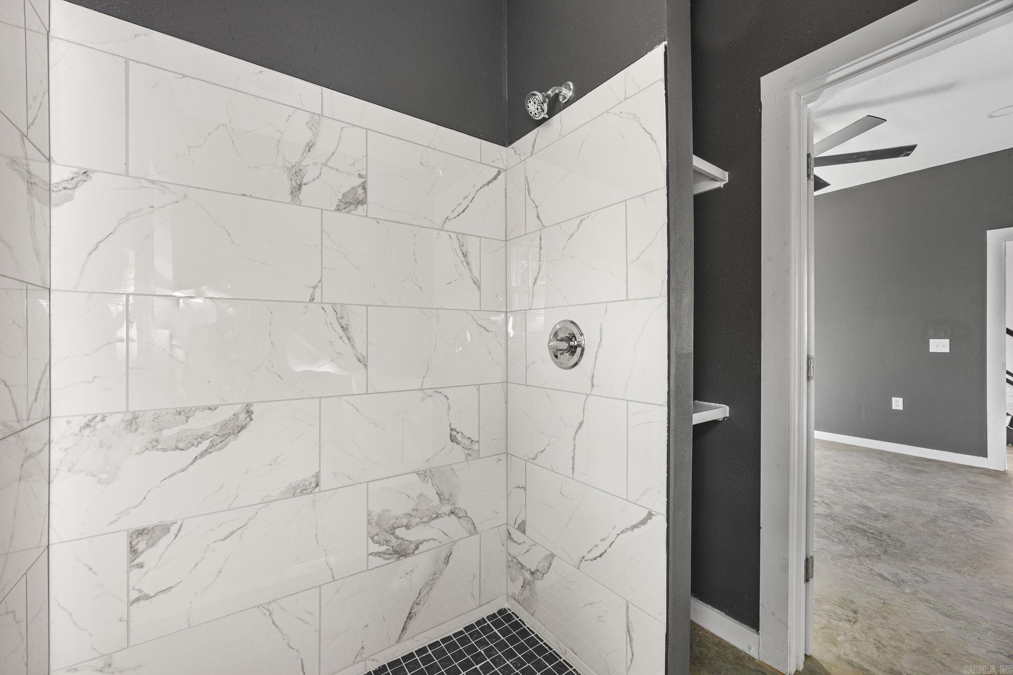 Walk-in shower with white marble-look tile, black floor tile, and chrome fixtures.