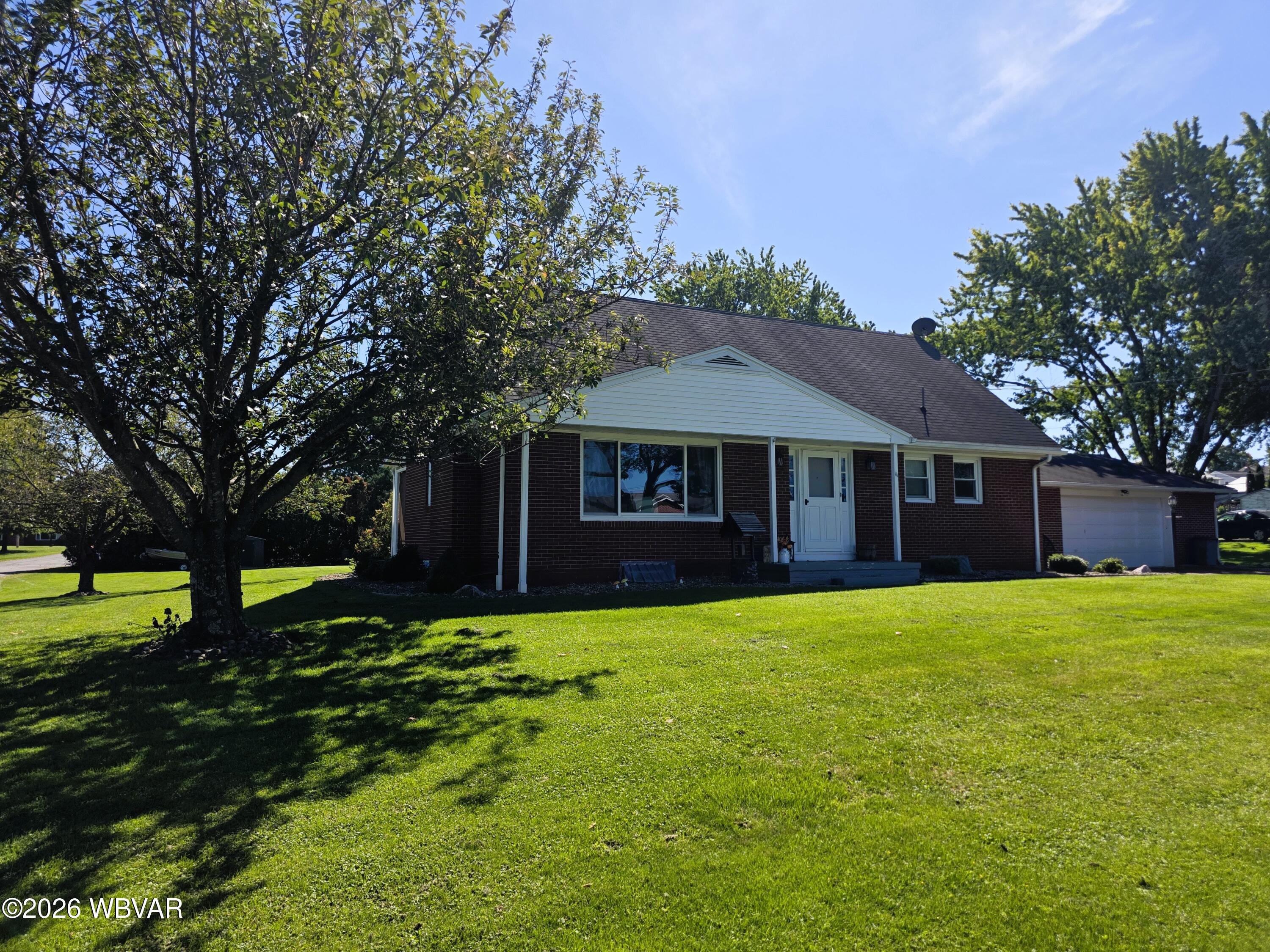 Brick ranch house with attached garage, white front gable, broad lawn, and mature shade trees.