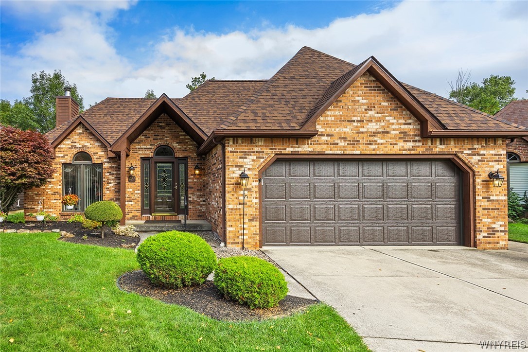 Brick house with a brown gabled roof, dark double garage door, and landscaped front lawn.