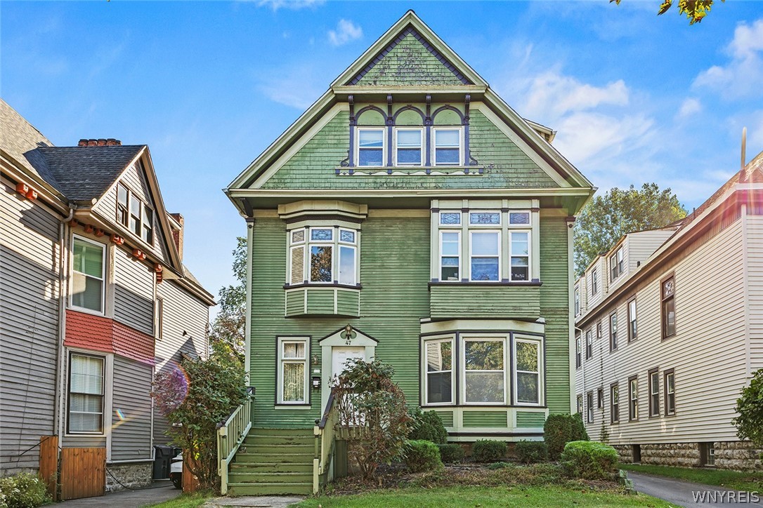 Green Victorian house with a steep gable, bay windows, and front steps between neighboring homes.