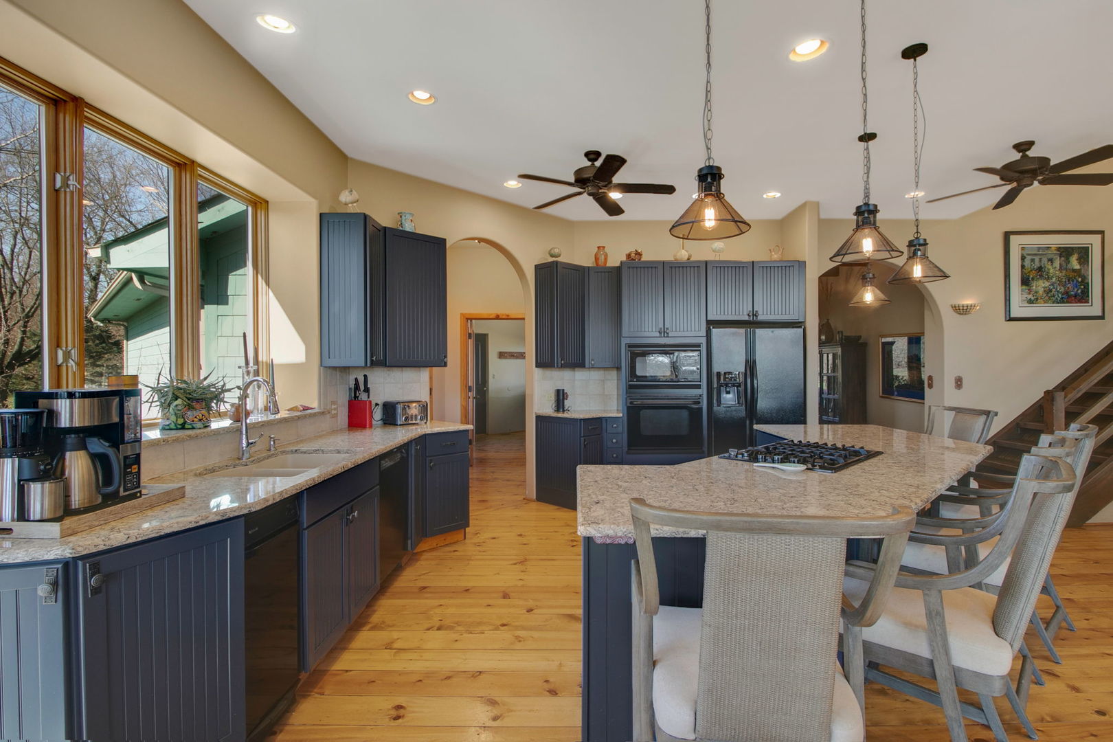 Kitchen with dark blue cabinets, granite island and cooktop, and wide windows overlooking trees.