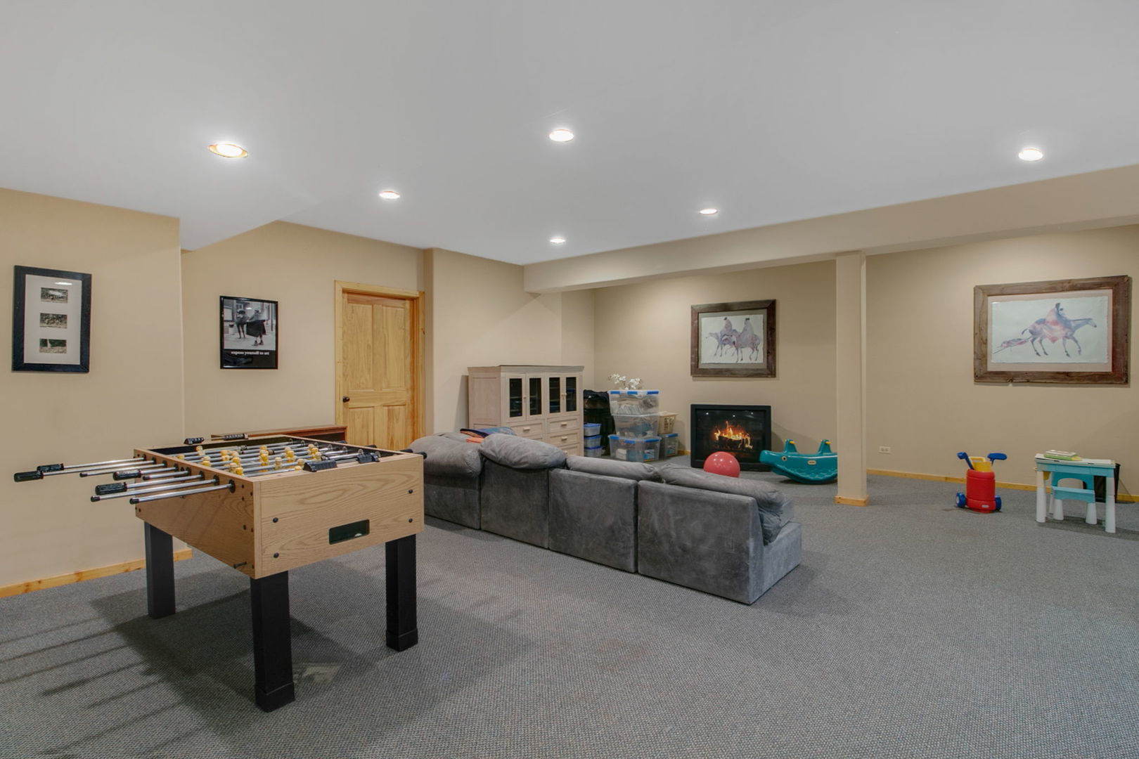 Basement recreation room with a foosball table, sectional sofa, and lit fireplace.