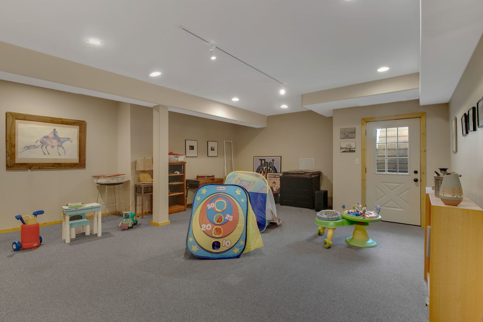 Finished basement playroom with a colorful children’s tent, toys, gray carpet, and a glass-paneled door.