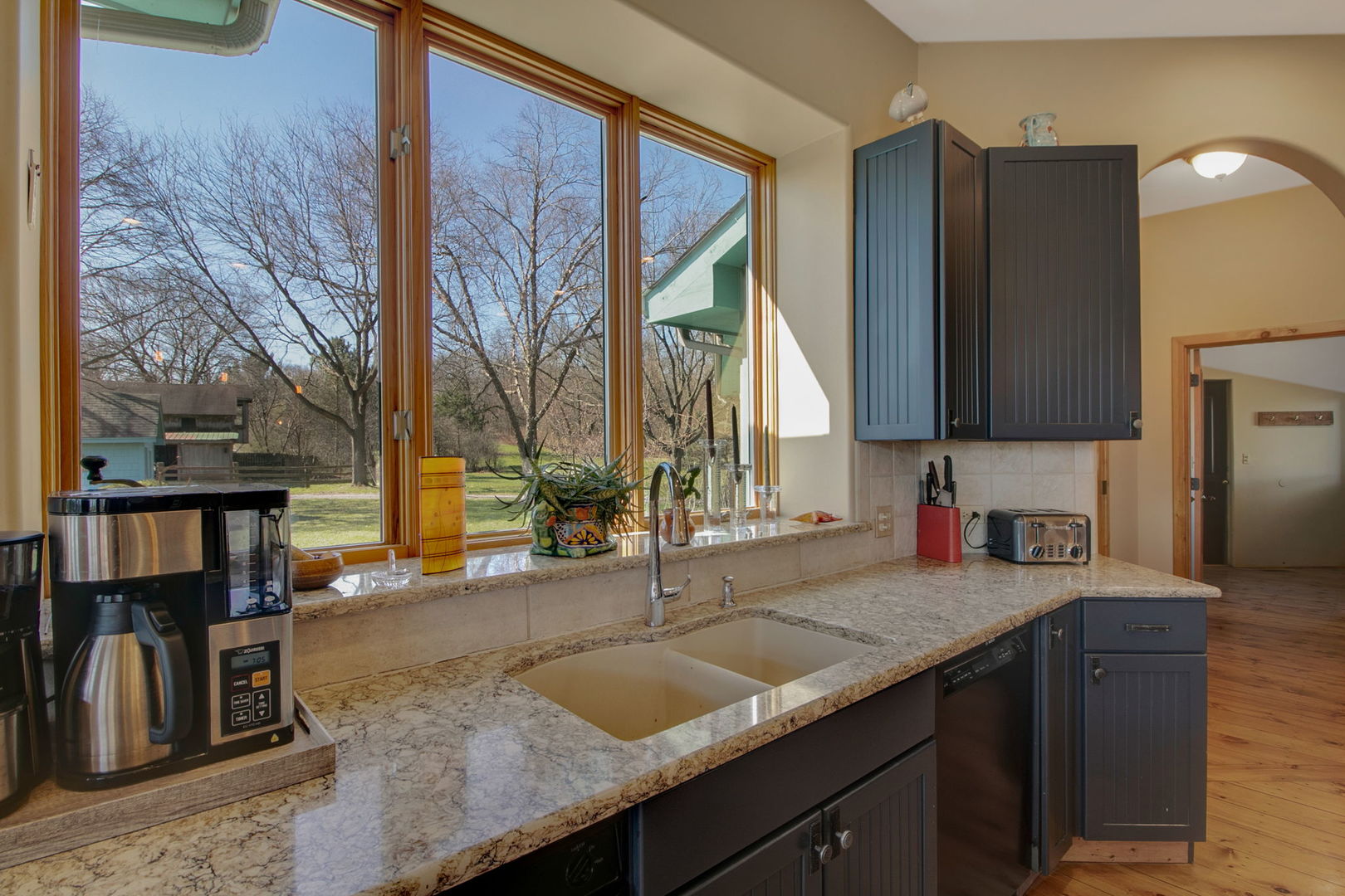 Kitchen with granite counters, dark cabinets, and wide windows overlooking a yard.