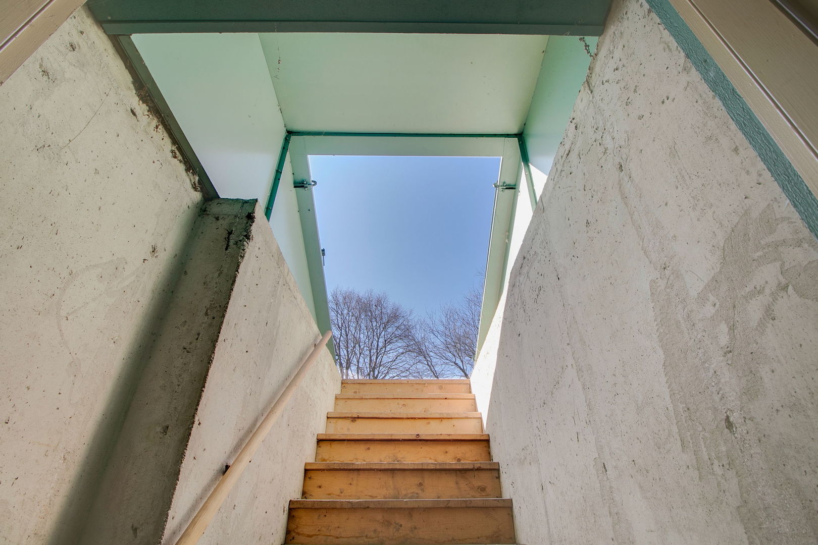 Unfinished concrete stairwell with wooden steps leading to an open exit beneath a blue sky.