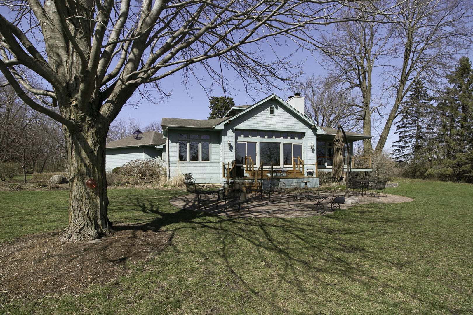 Teal home with a raised deck and patio furniture, framed by a large leafless tree.