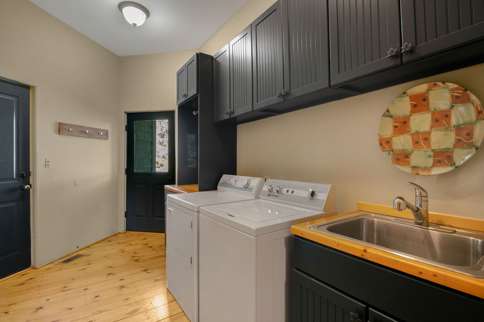 Laundry room with washer, dryer, utility sink, dark cabinets, and wood flooring.