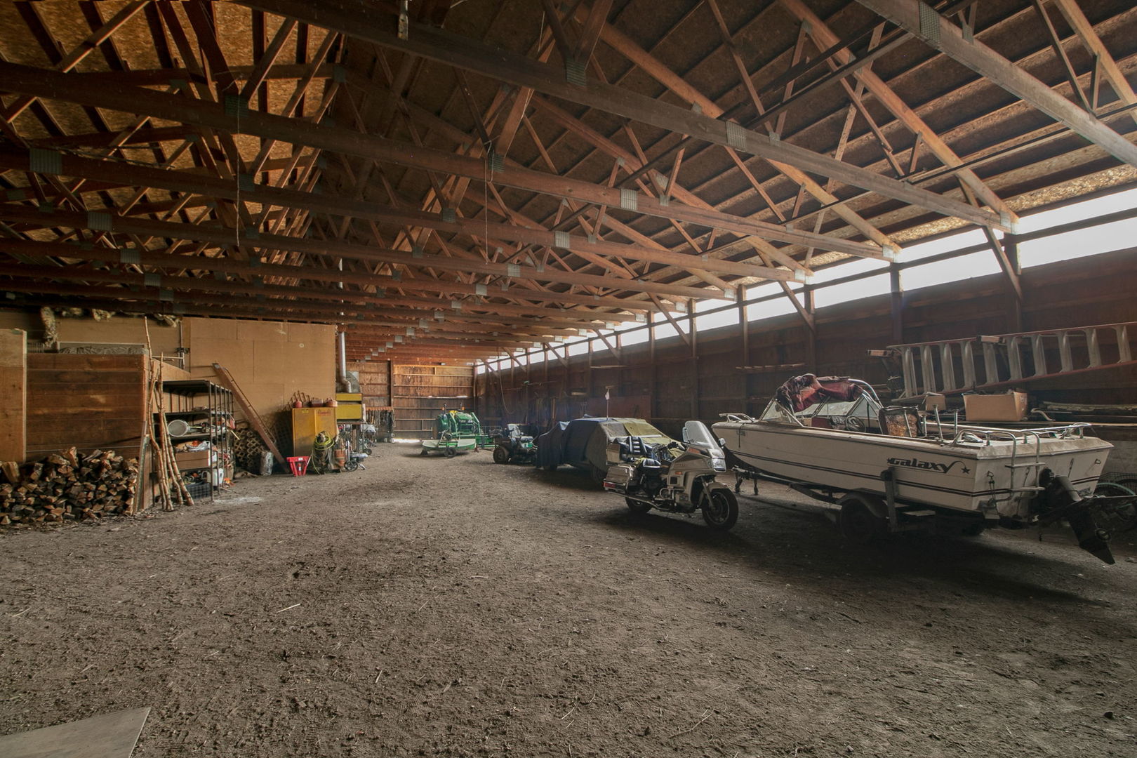 Large timber-framed barn interior with a boat, equipment, and dirt floor.