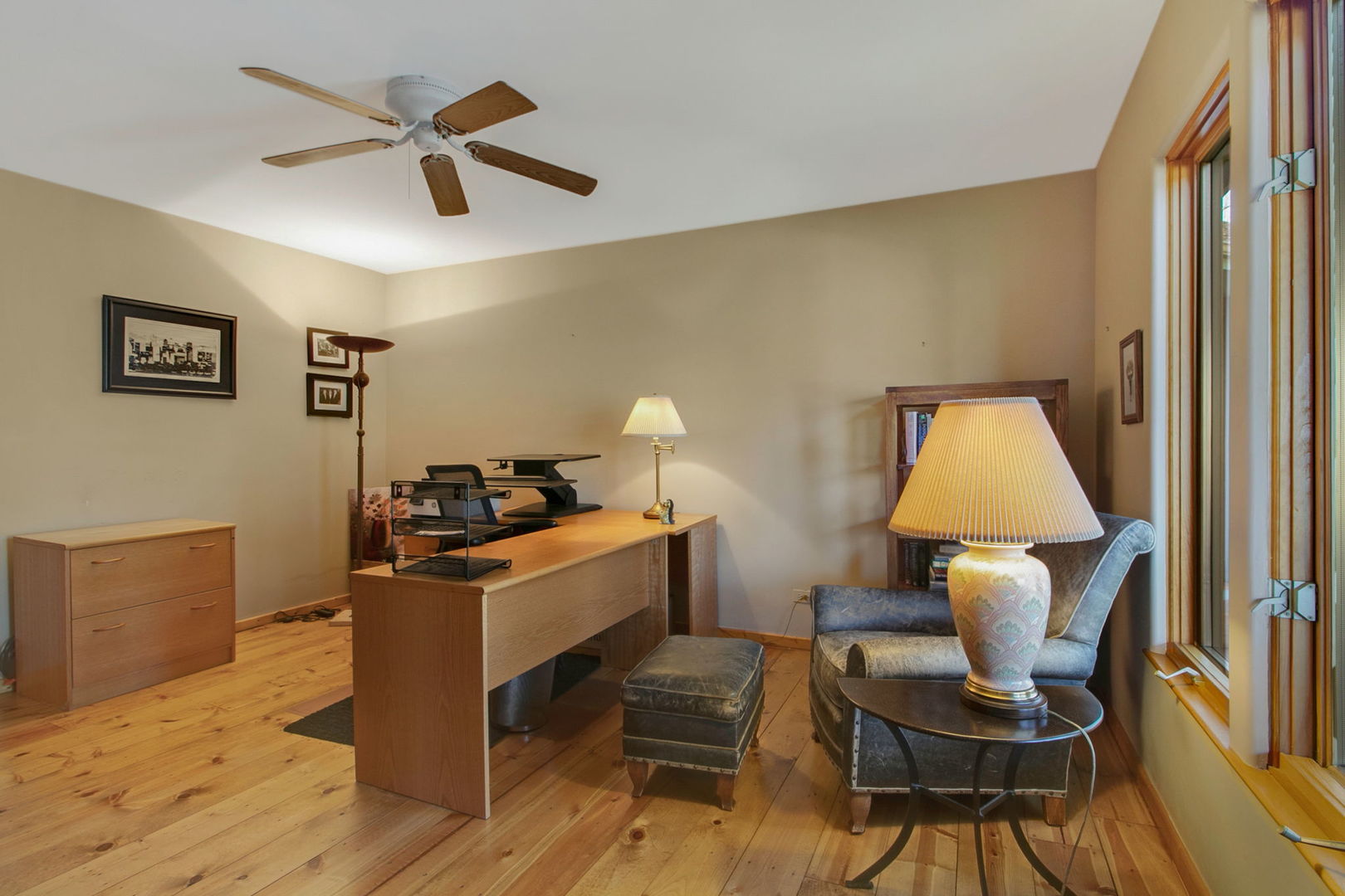 Home office with a wooden desk and a reading nook beside tall windows.