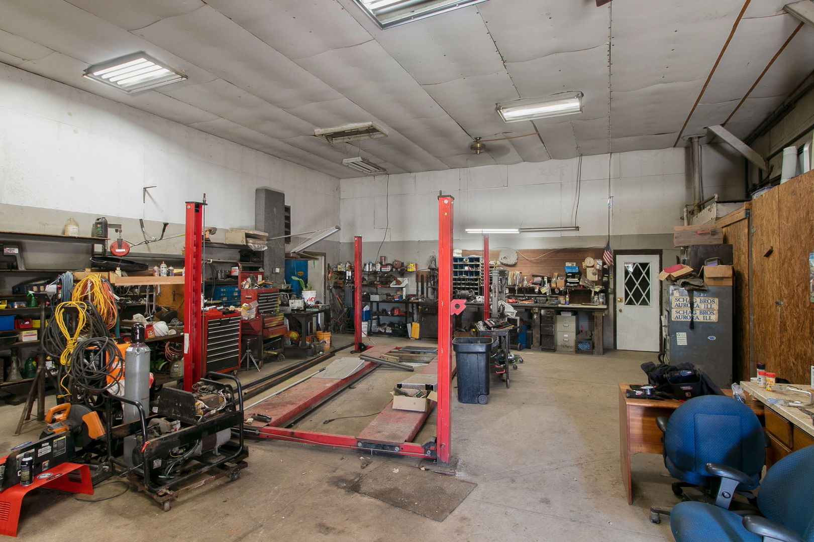 Workshop garage with a red vehicle lift, crowded tool benches, and a concrete floor.