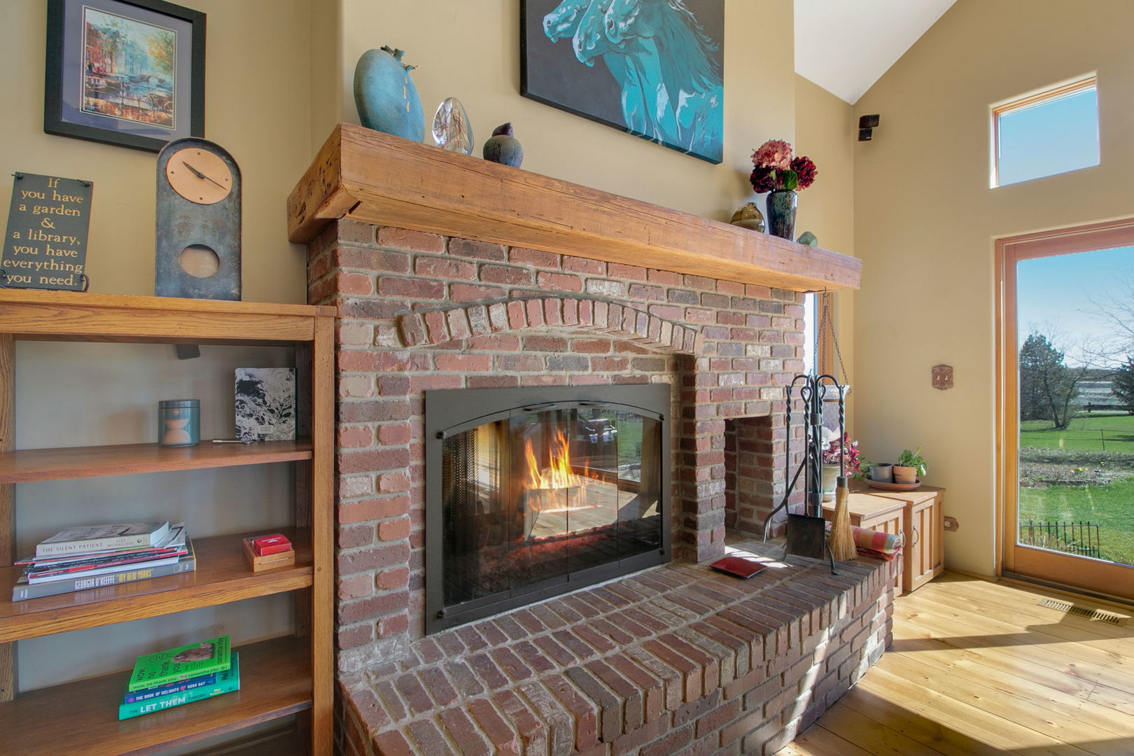 Living room fireplace with a brick surround, wooden mantel, and built-in shelving beside a glass door.