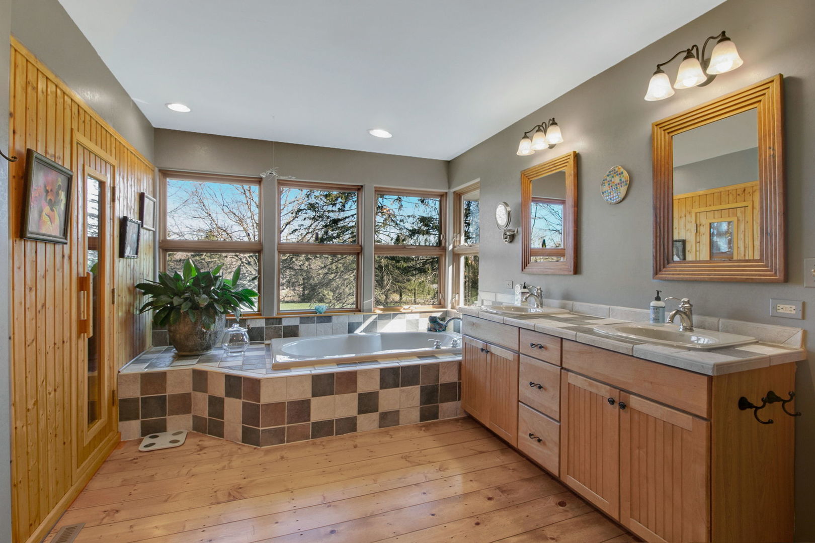 Bathroom with a tiled soaking tub beneath large windows and a long double-sink vanity.
