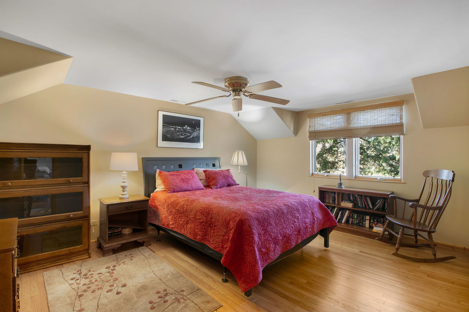 Bedroom with a red quilted bed, sloped ceiling, and hardwood floors.
