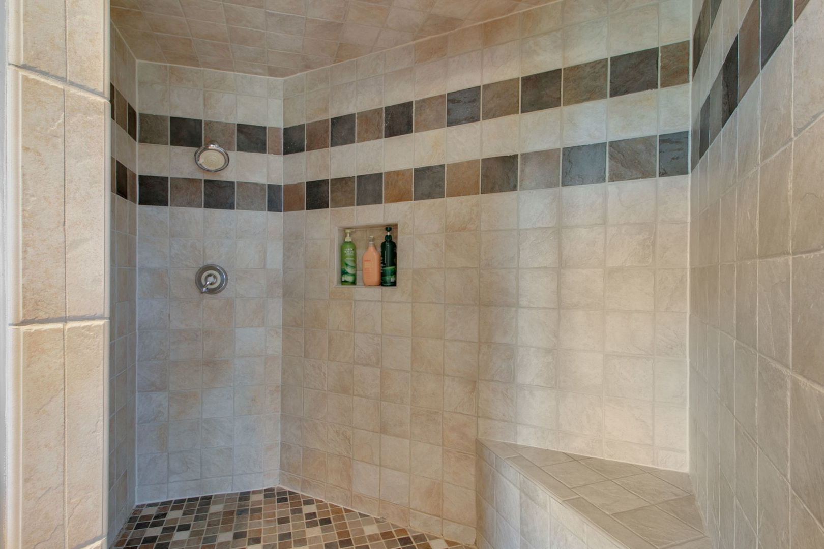 Tiled walk-in shower with a built-in bench, recessed niche, and multicolored accent band.